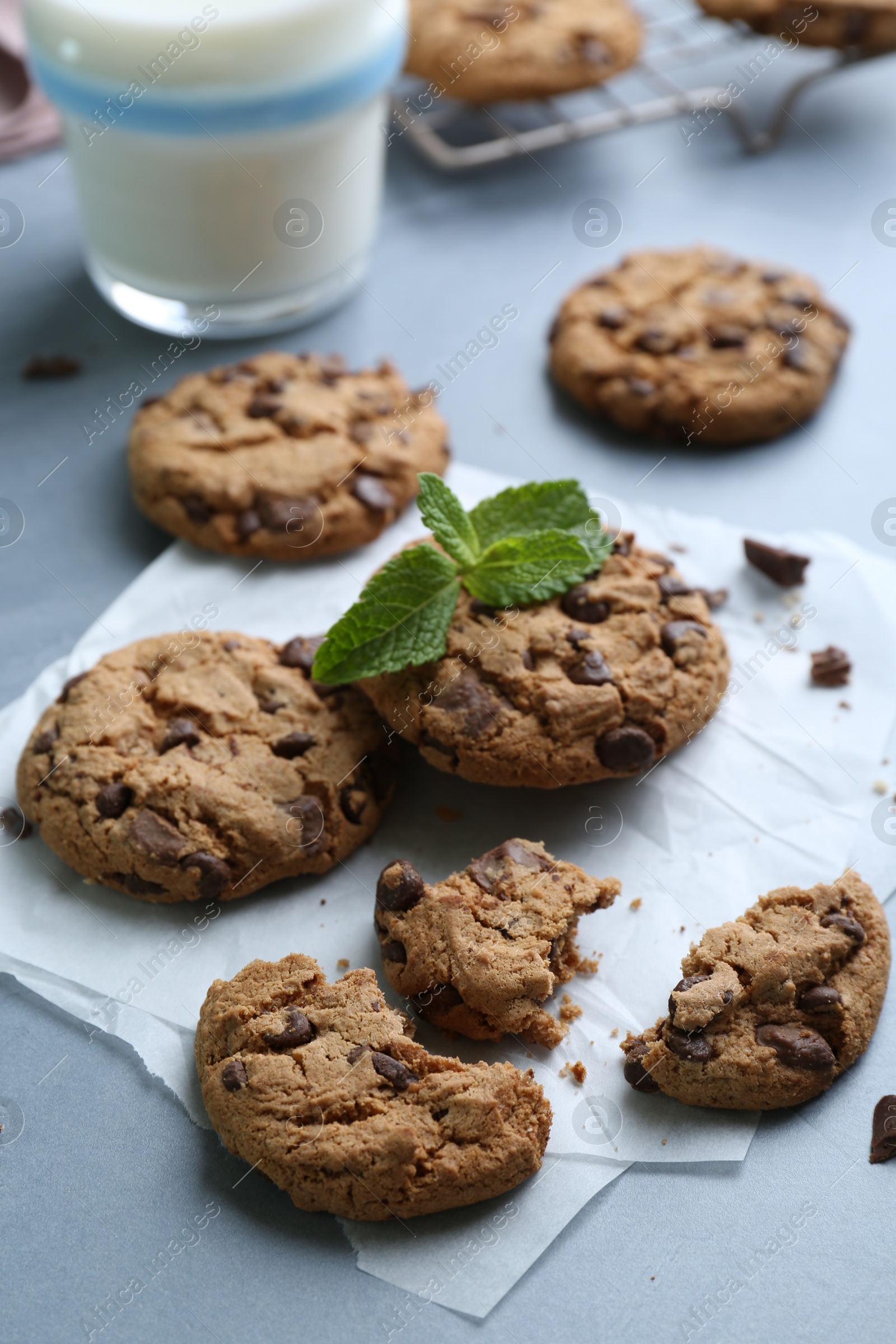 Photo of Tasty chocolate chip cookies, glass of milk and mint leaves on light grey table