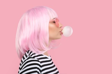 Photo of Beautiful woman in sunglasses blowing bubble gum on pink background, space for text