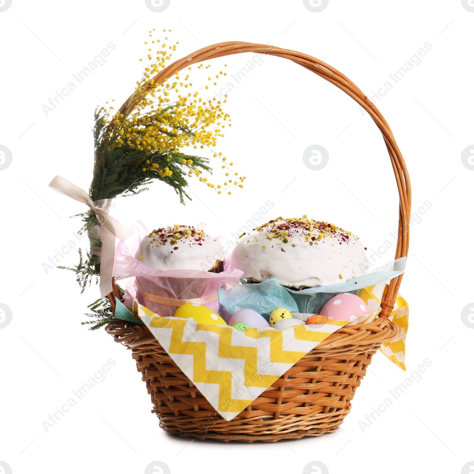 Photo of Basket with delicious Easter cakes, dyed eggs and flowers on white background