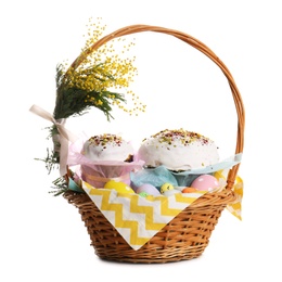 Photo of Basket with delicious Easter cakes, dyed eggs and flowers on white background