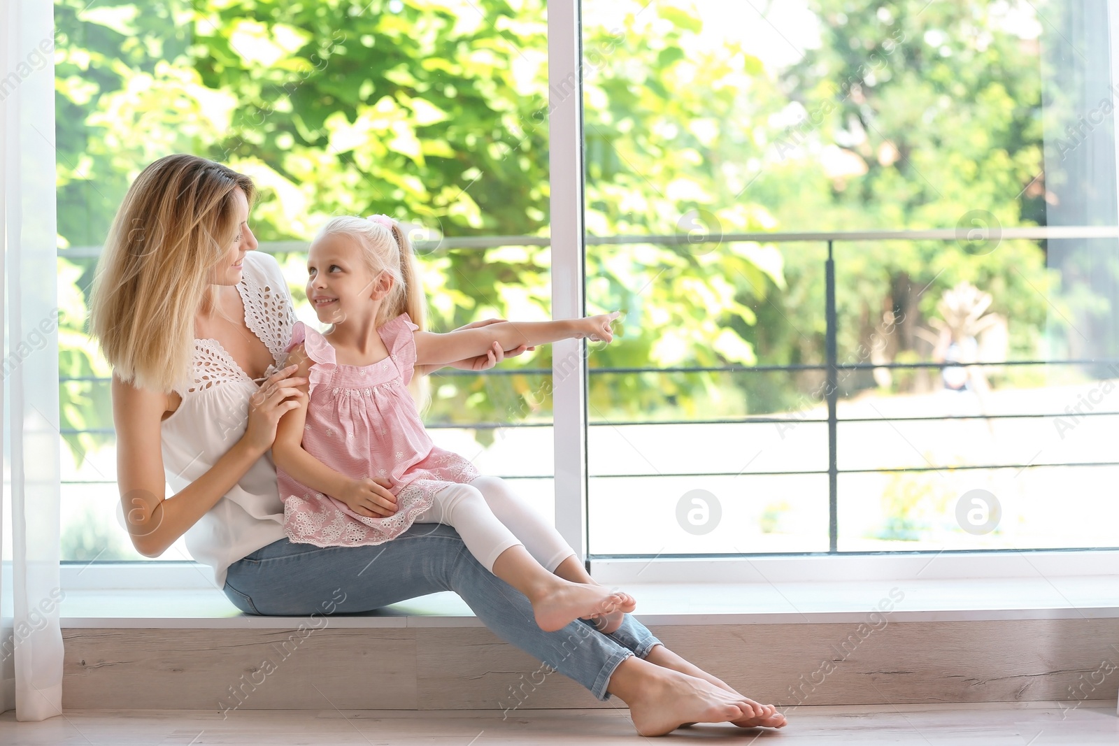 Photo of Young woman with cute little girl near window at home