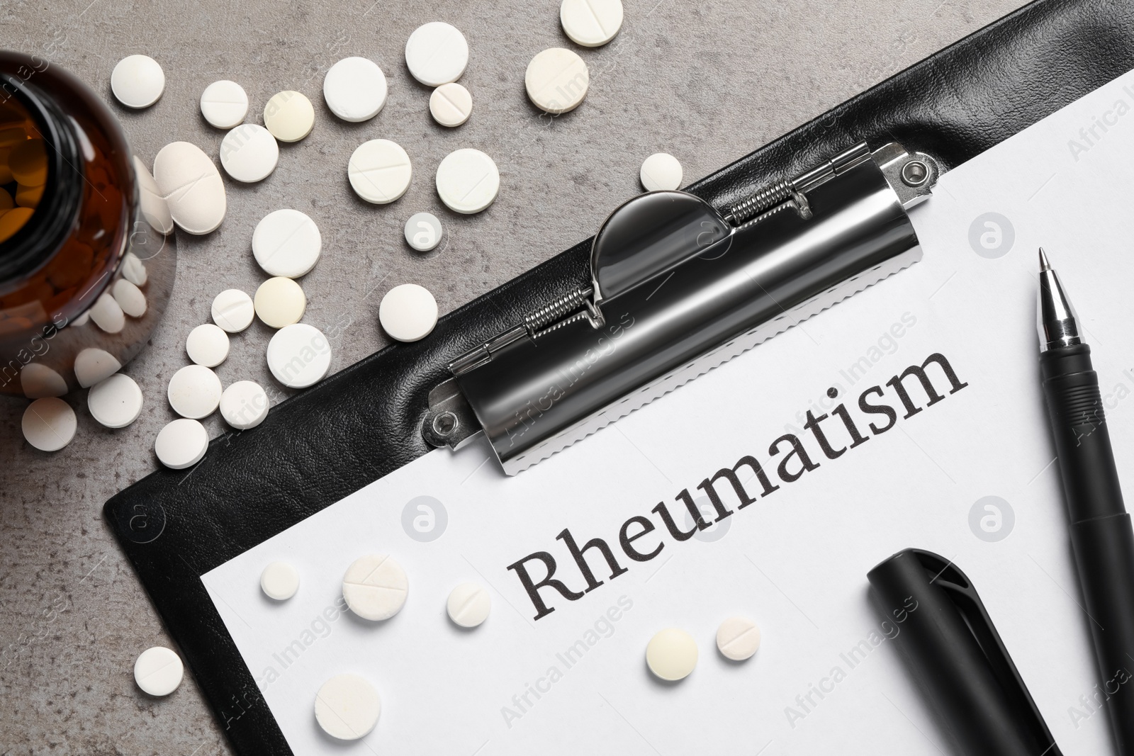 Photo of Clipboard with word Rheumatism and pills on light gray textured background, flat lay