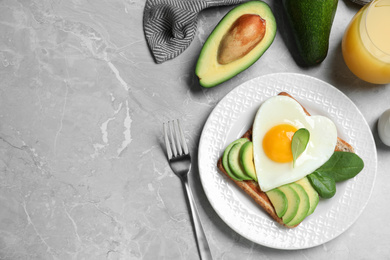 Photo of Tasty breakfast with heart shaped fried egg served on  grey table, flat lay