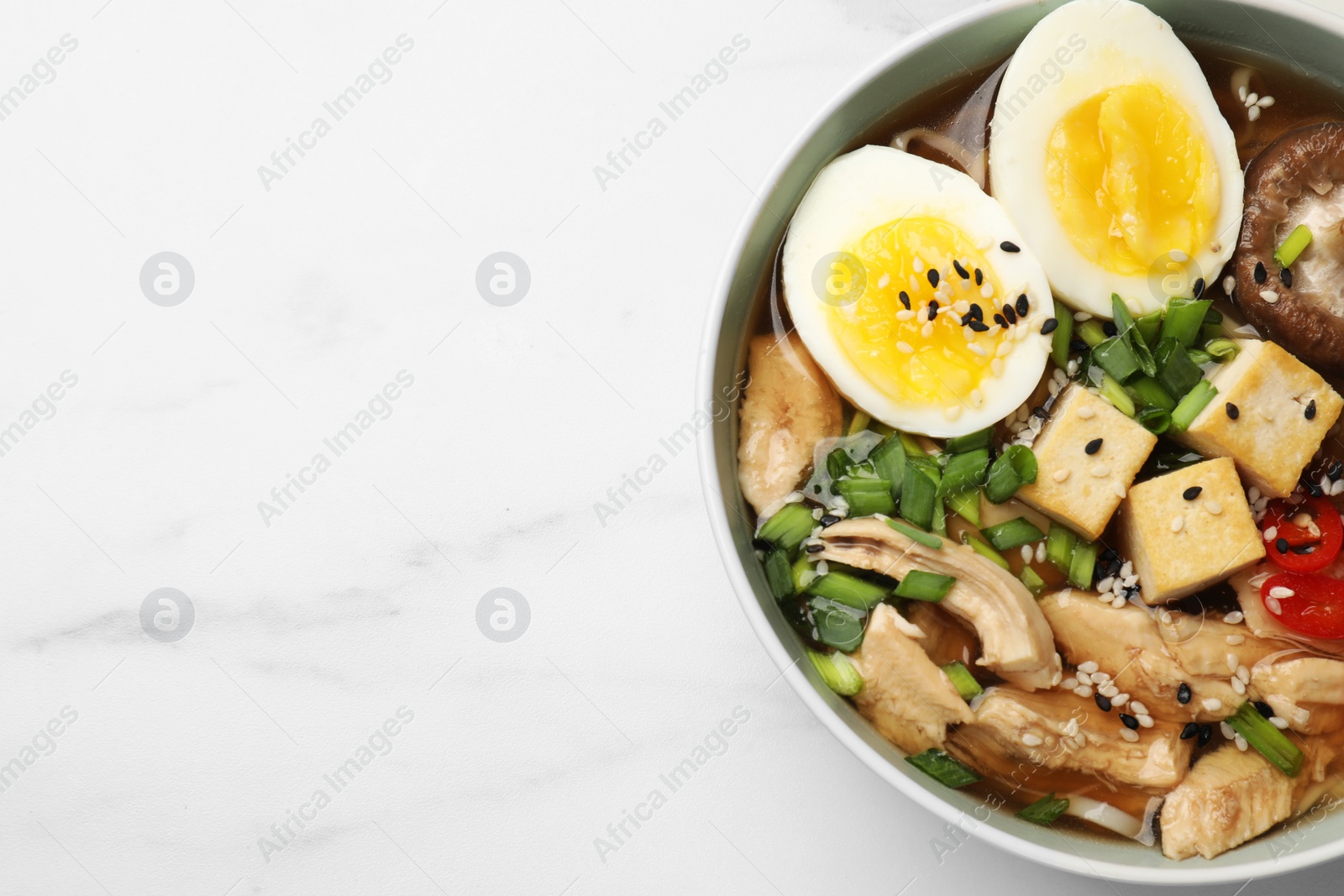 Photo of Bowl of delicious ramen on white marble table, top view with space for text. Noodle soup