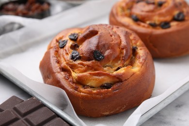 Photo of Delicious rolls with raisins and chocolate bar on white table. Sweet buns