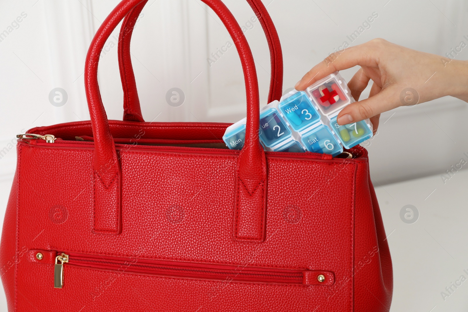 Photo of Woman putting pill box into bag indoors, closeup