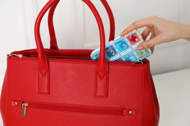 Woman putting pill box into bag indoors, closeup