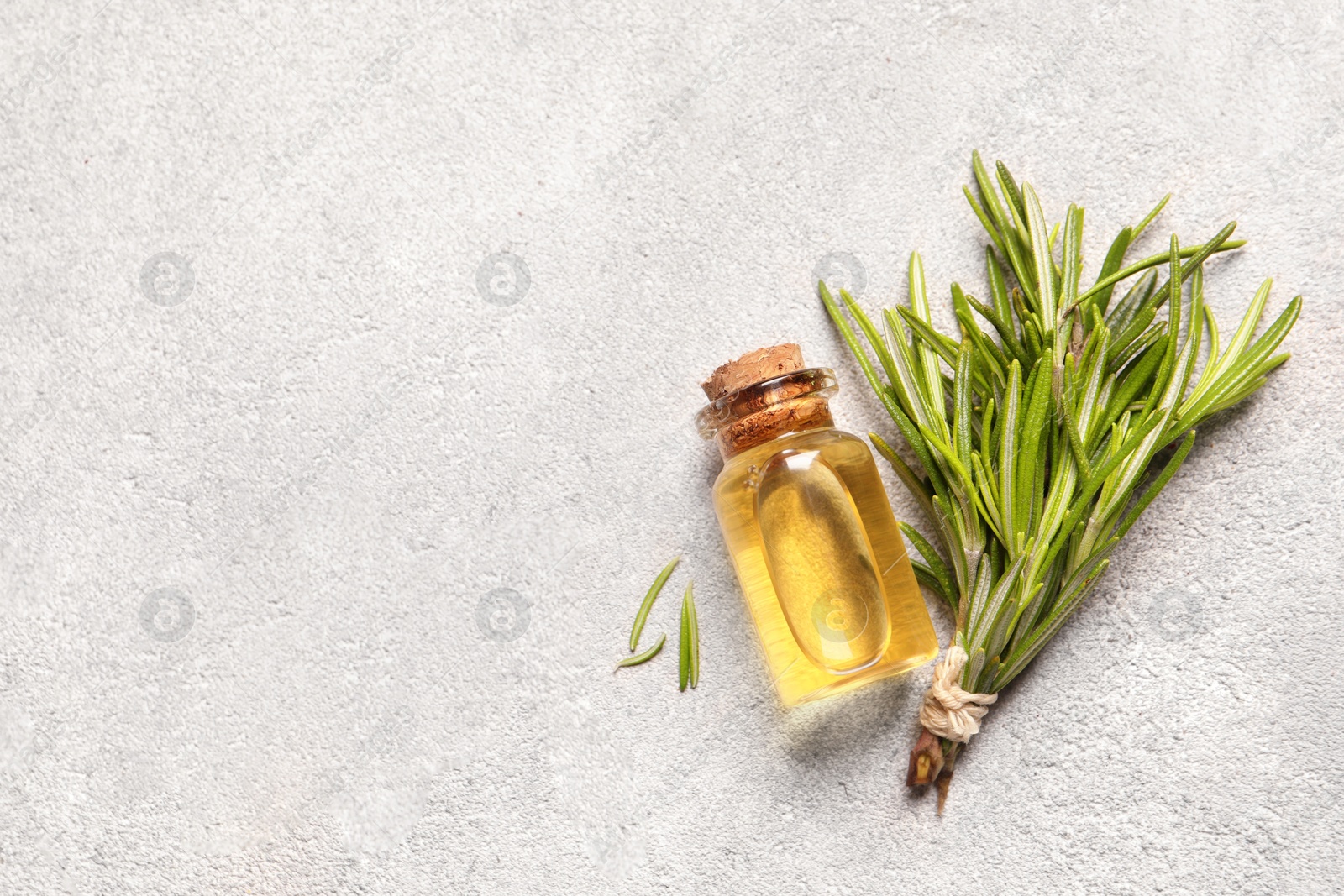 Photo of Bottle with essential oil and fresh rosemary on light textured table, flat lay. Space for text