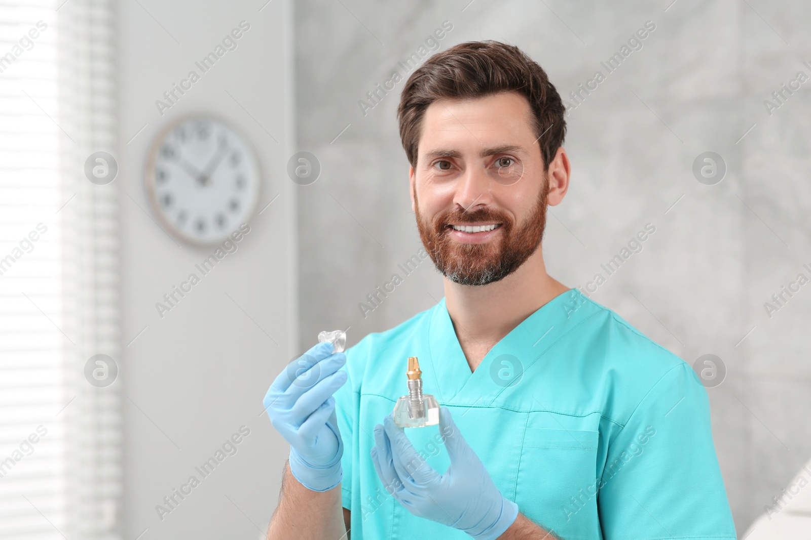 Photo of Dentist holding educational model of dental implant in clinic. Space for text