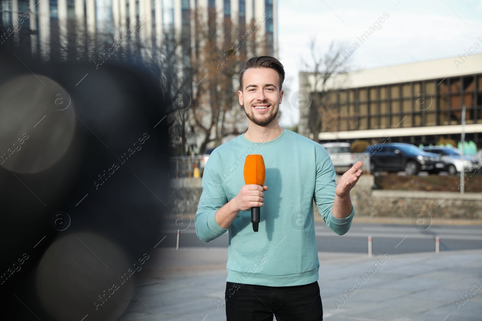 Photo of Young male journalist with microphone working on city street