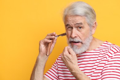Photo of Senior man shaving beard with blade on orange background, space for text