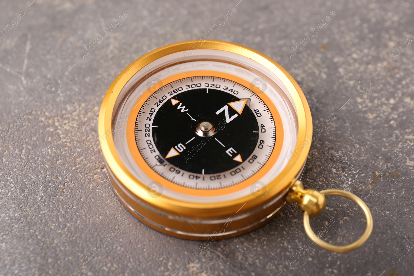 Photo of One compass on grey textured background, closeup. Navigation equipment