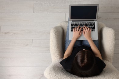 Photo of Woman working with laptop in armchair, top view. Space for text