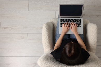 Woman working with laptop in armchair, top view. Space for text