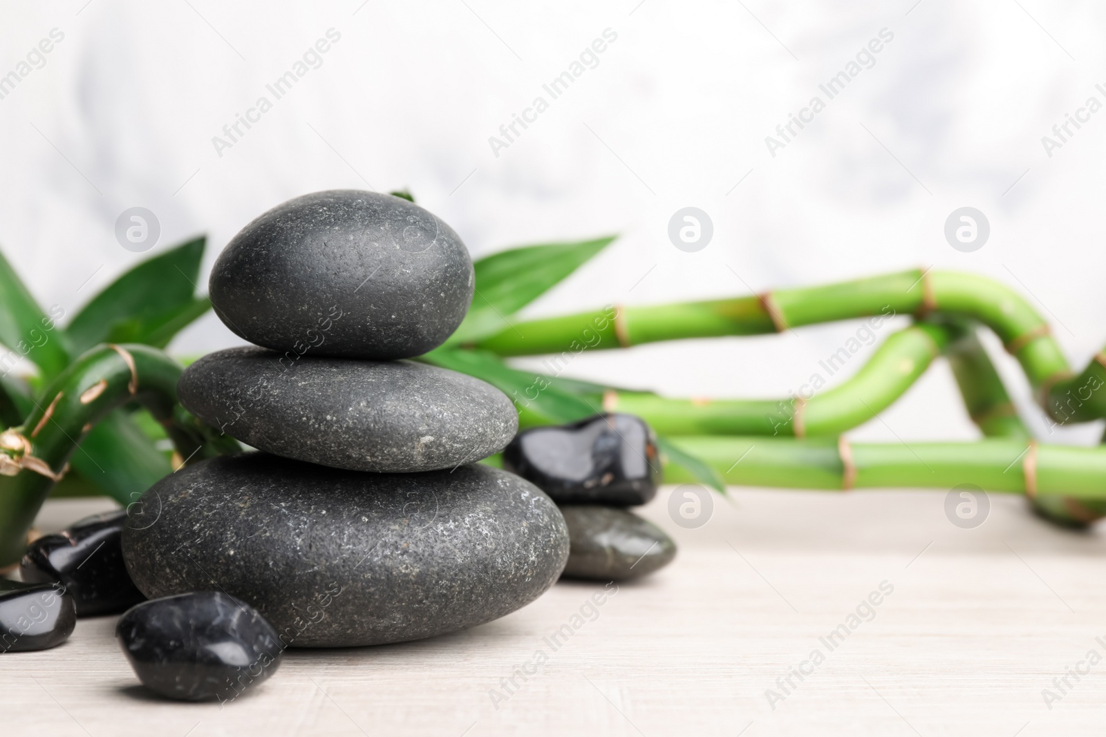 Photo of Stacked spa stones and bamboo on white wooden table. Space for text