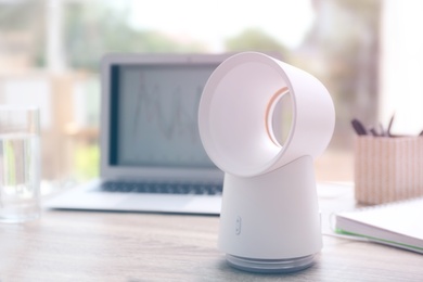 Modern portable fan on wooden table in office, space for text. Summer heat