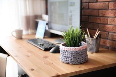 Photo of Knitted flowerpot cover with plant on office table, space for text. Interior element