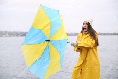 Photo of Woman in yellow raincoat with umbrella caught in gust of wind near river