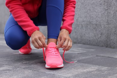 Woman in gym clothes tying shoelace of sneakers on street, closeup. Space for text