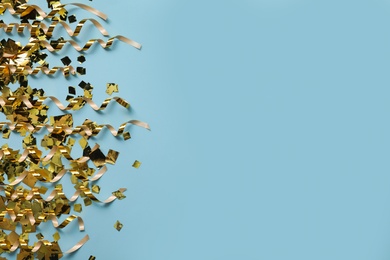 Shiny golden serpentine streamers and confetti on light blue background, flat lay. Space for text