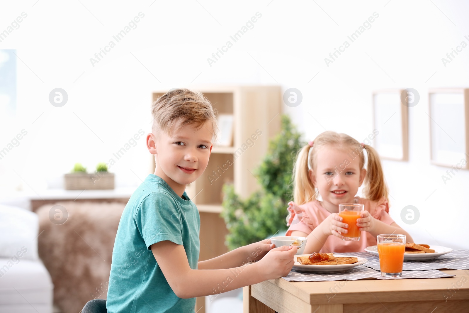 Photo of Adorable little children eating tasty toasted bread with jam at table