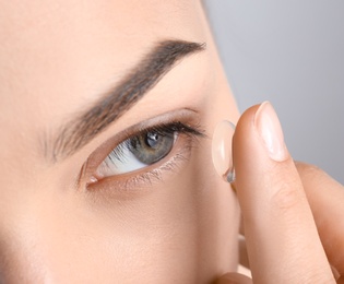 Young woman putting contact lens in her eye, closeup