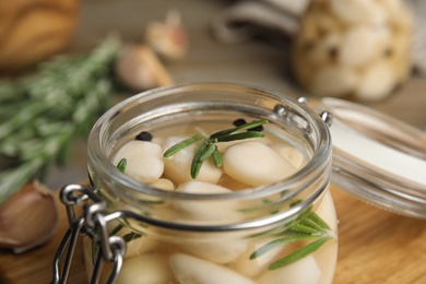 Photo of Jar of pickled garlic on wooden table, closeup