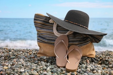 Photo of Beautiful hat, bag and flip flops near sea on pebble beach