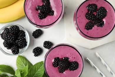 Delicious blackberry smoothie in glasses and ingredients on marble table, flat lay