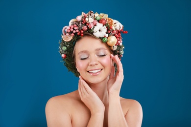 Photo of Beautiful young woman wearing Christmas wreath on blue background