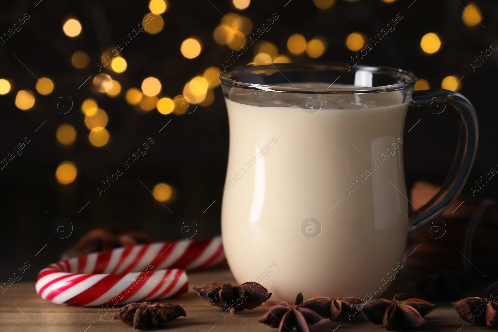 Photo of Glass of delicious eggnog with anise stars and candy cane on wooden table