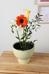 Photo of Stylish ikebana as house decor. Beautiful fresh flowers and branch on wooden table near white wall