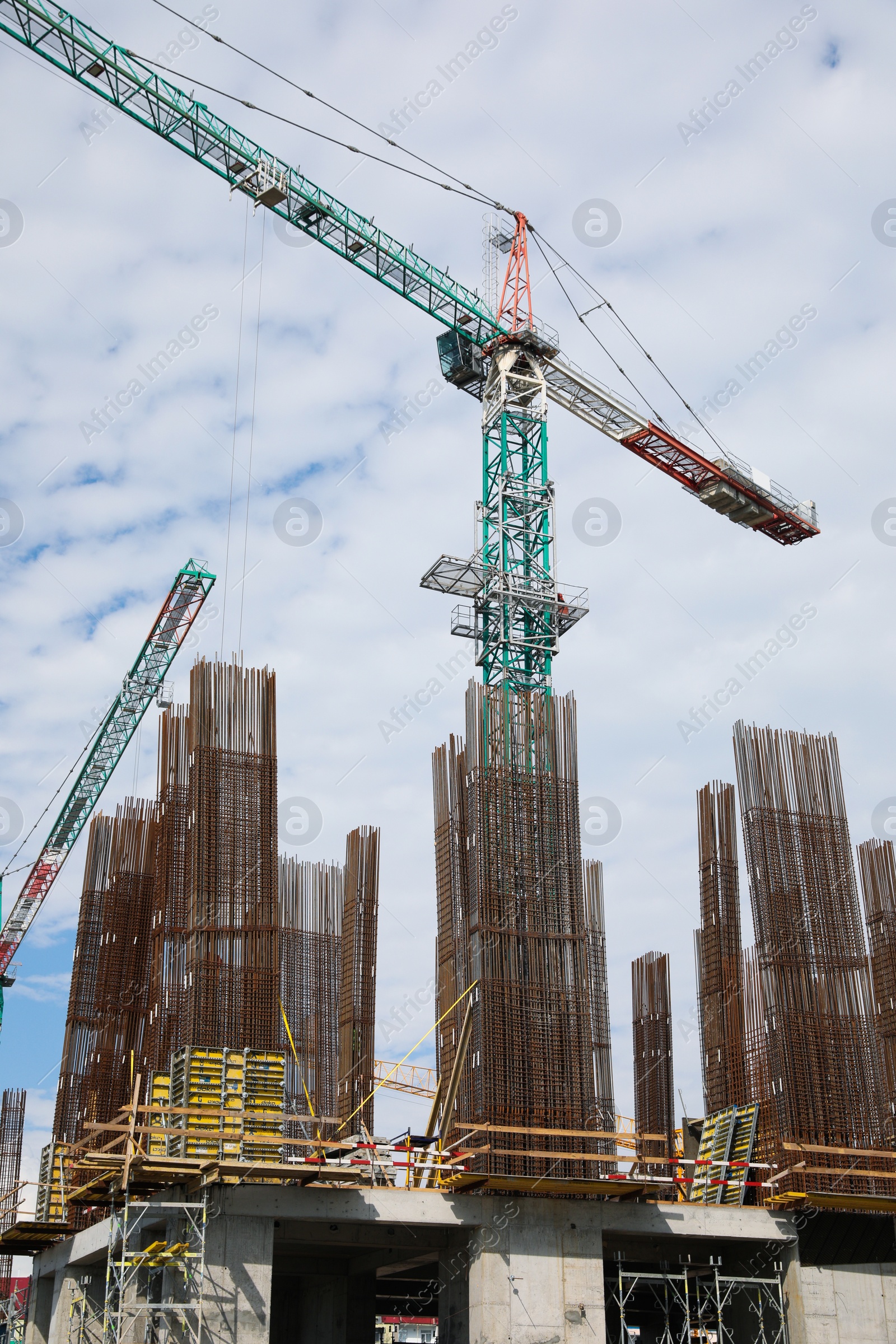 Photo of Tower crane near building under construction against cloudy sky