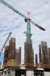 Tower crane near building under construction against cloudy sky
