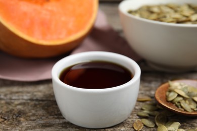 Photo of Bowl of pumpkin oil and seeds on wooden table, closeup