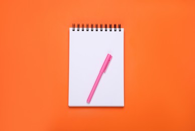 Blank office notebook and pen on orange background, top view