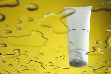 Moisturizing cream in tube on glass with water drops against yellow background, low angle view. Space for text