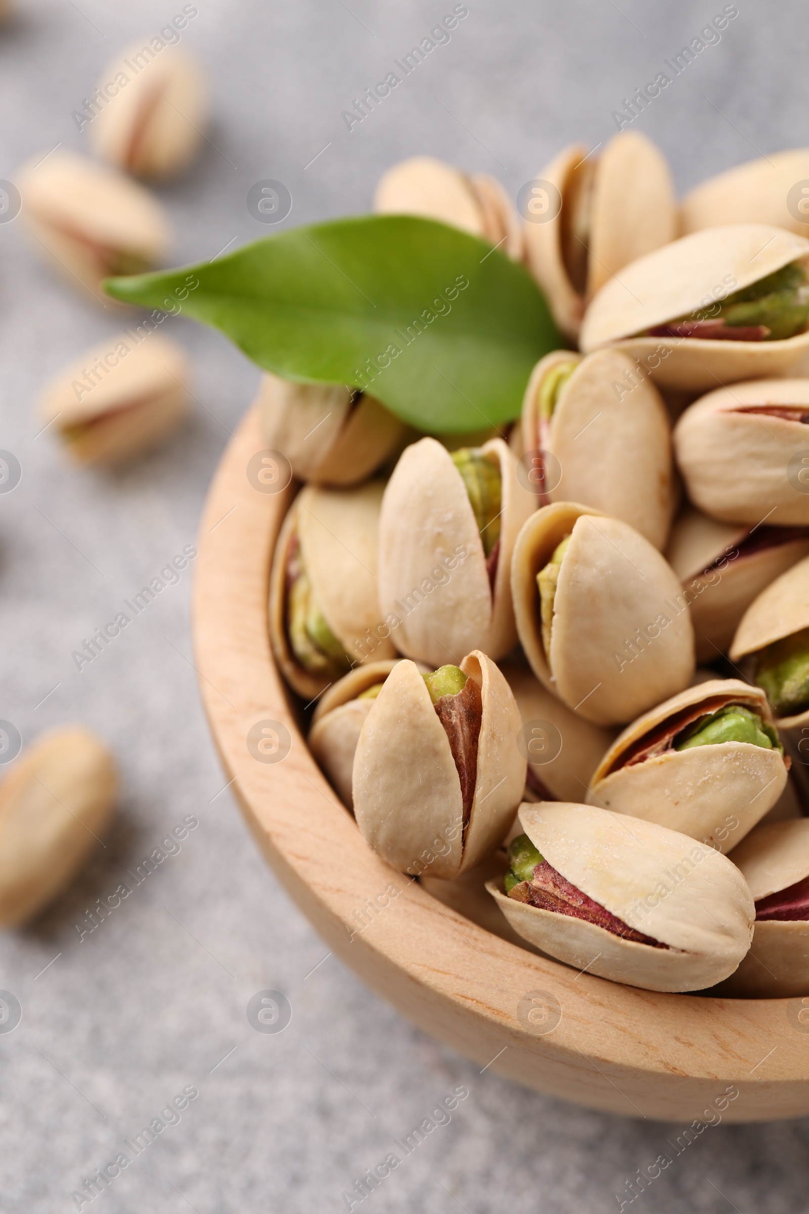 Photo of Delicious pistachios in bowl on grey textured table, closeup