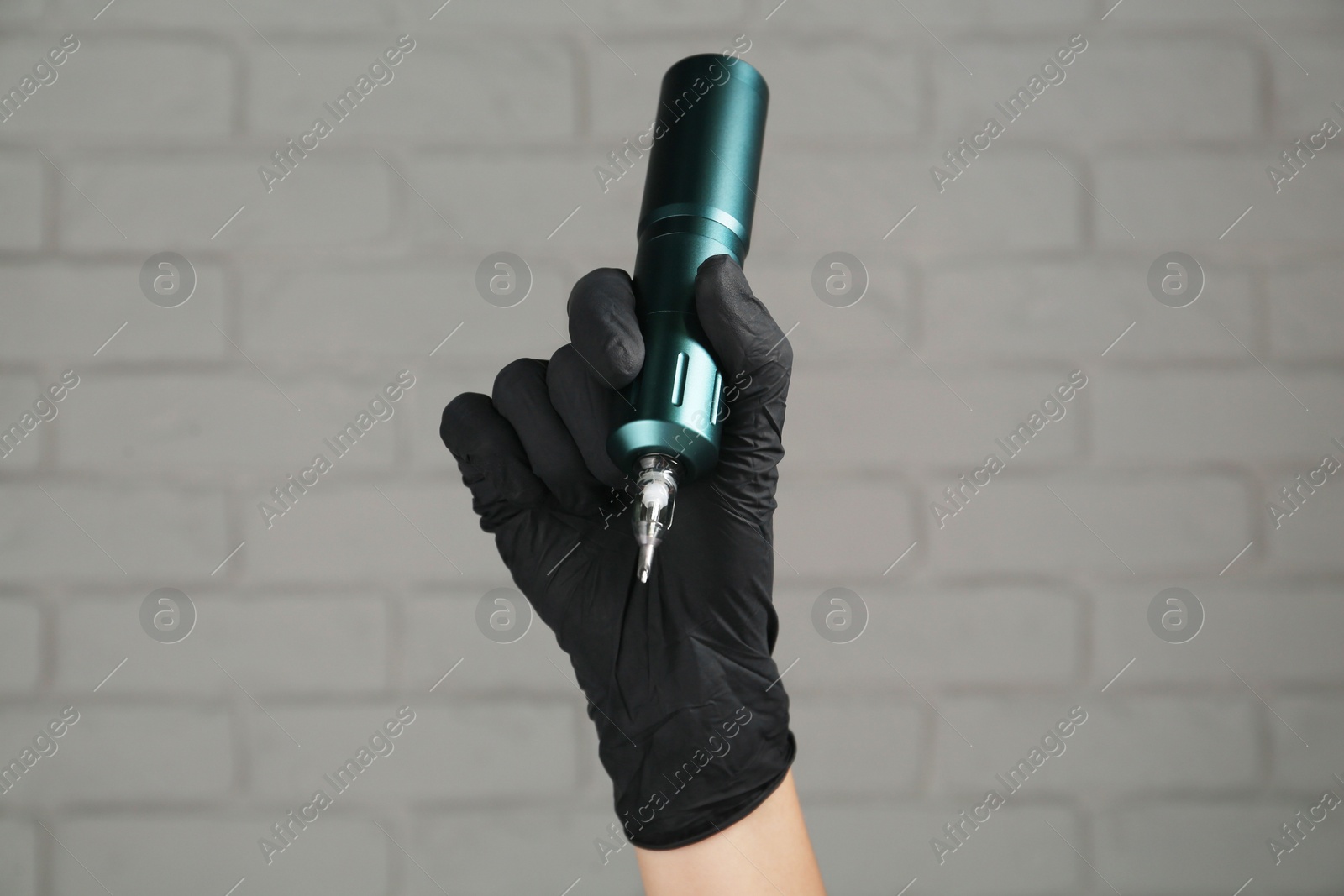 Photo of Professional tattoo artist with machine near white brick wall, closeup