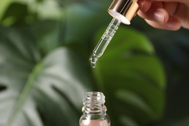 Photo of Woman dripping cosmetic serum from pipette into bottle on blurred background, closeup