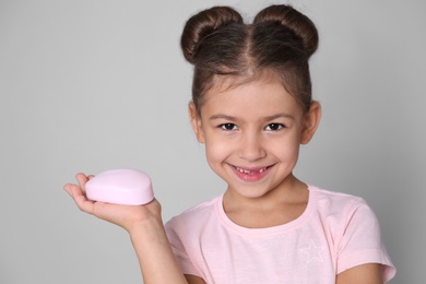 Cute little girl with soap bar on gray background