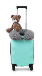 Photo of Soft travel pillow and toy bear on turquoise suitcase isolated on white