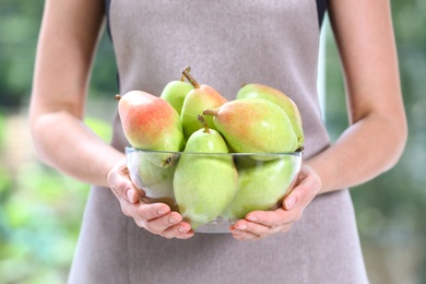 Woman holding fresh ripe pears against blurred background, closeup