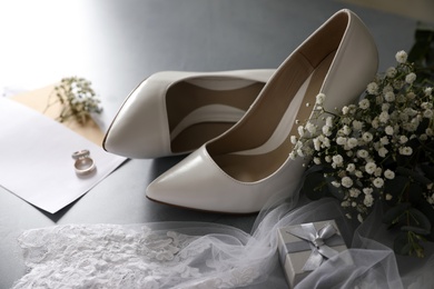 Photo of Composition with wedding bouquet, white high heel shoes and veil on grey background