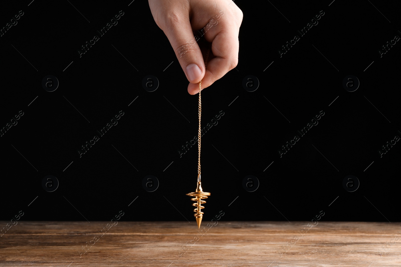 Photo of Psychotherapist with pendulum on black background, closeup. Hypnotherapy session