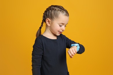 Little girl with smart watch on yellow background