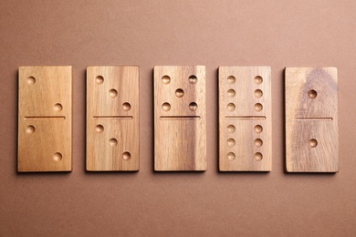 Photo of Wooden domino tiles on brown background, flat lay