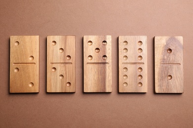 Wooden domino tiles on brown background, flat lay