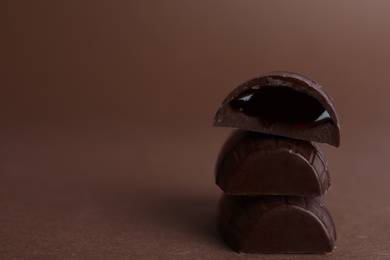 Photo of Tasty dark chocolate candies with jelly filling on brown table, closeup. Space for text