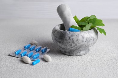 Photo of Marble mortar with fresh green herbs and pills on white table, closeup